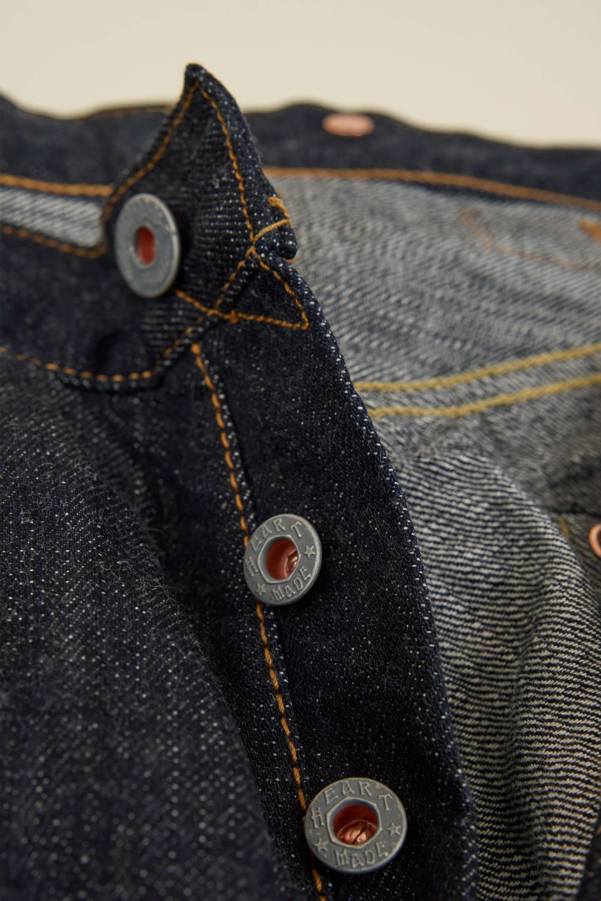 Graph Zero Heritage Denim - 13oz close-up of embossed metal buttons and selvedge denim fabric details.